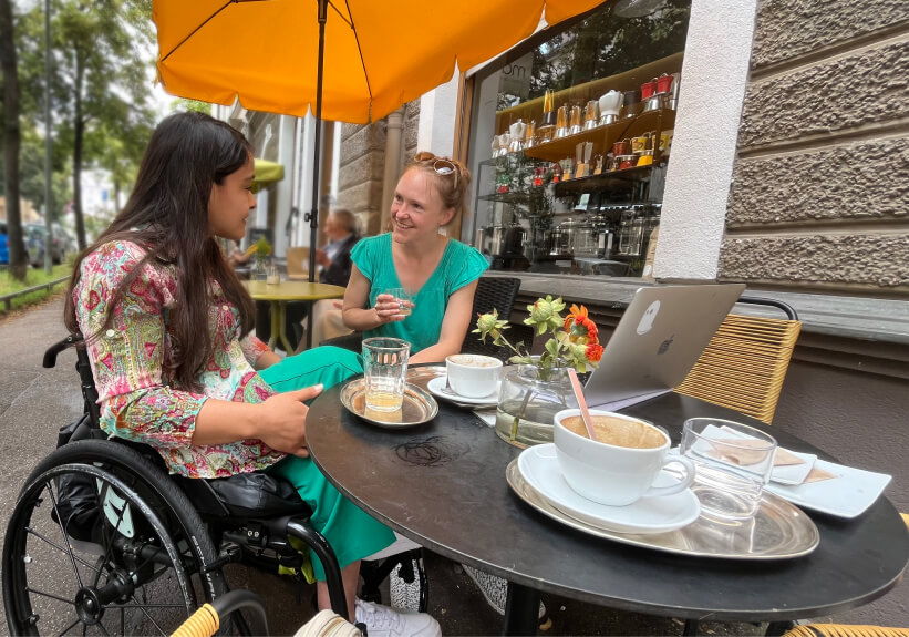 2 Freundinnen im Café. Eine der Frauen sitzt im Rollstuhl.