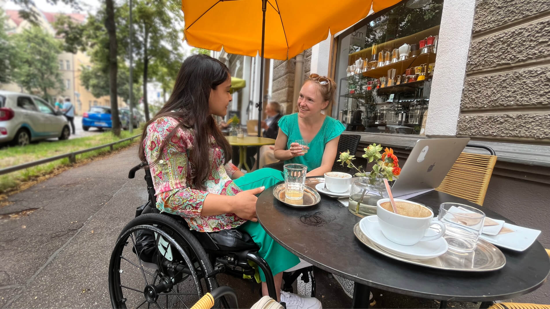 2 Freundinnen im Café. Eine der Frauen sitzt im Rollstuhl.